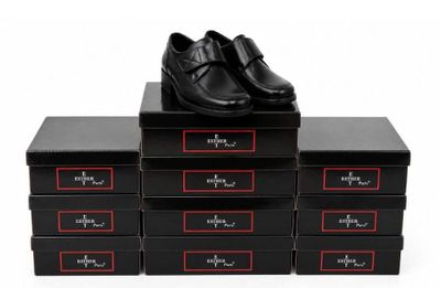 quatre boîtes noires posées sur une surface blanche, avec des chaussures noires posées dessus