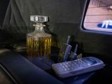 a bottle of alcohol and a cell phone on a tray in the back seat of a car