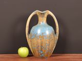 a blue and brown vase sitting on a table next to a green apple