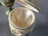 a small white box with pearls on it and an egg in the background