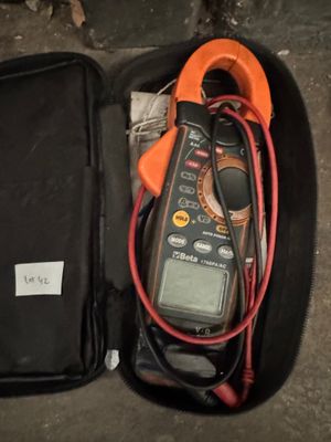 un multimètre dans un étui posé par terre à côté d'un sac noir