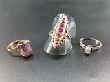 three rings and a ring with a pink stone on a black surface
