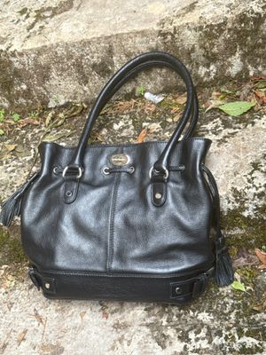 un sac à main noir posé par terre près d'un mur de pierre