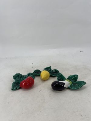 two small figurines of fruits and leaves on a white surface