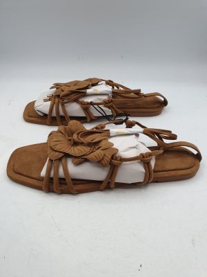 une paire de sandales marron à semelles blanches posées sur une surface blanche