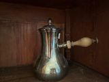 une cafetière en argent avec une poignée en bois, posée sur une étagère