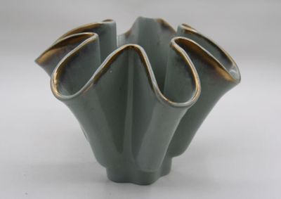 a green vase with a gold rim sitting on a white surface