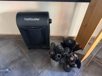 a black hair dryer sitting on the floor next to a bunch of hair brushes