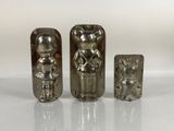 three silver metal figurines sitting on top of a white surface