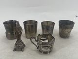 four silver cups and spoons sitting next to each other on a white surface