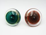 une paire d'yeux en verre verts et rouges posés sur une surface blanche