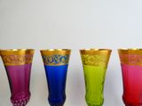 four different colored glass vases are lined up against a white background