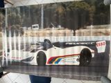 un homme tenant une photo d'une voiture de course devant une clôture grillagée