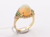 a close up of a ring with a white opal and green stones