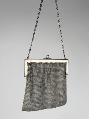 a silver mesh purse hanging from a chain on a gray background