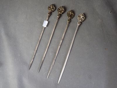 four antique silverware spoons with ornate handles on a gray surface
