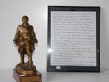 une statue en bronze représentant un homme tenant un livre à côté d'une photo encadrée