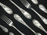 de nombreuses cuillères et fourchettes en argent posées sur une table noire