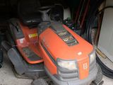 une tondeuse autoportée orange garée dans un garage, à côté d'un tas d'outils