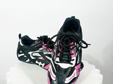 une paire de chaussures de course noires et roses posées sur un socle blanc