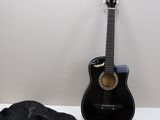 une guitare noire et un sac noir posés sur une table blanche