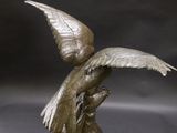 bronze sculpture of a bird on a branch with its wings spread