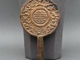 un ancien miroir chinois en bronze posé sur un socle, sur une surface grise