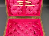 an open wooden box with pink fabric inside and a pair of knitting needles in it