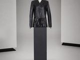mannequin vêtu d'une veste en cuir noir, posé sur un socle dans une pièce blanche