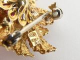 a close up of a gold brooch with a red stone