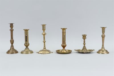 six brass candlesticks are lined up on a white surface