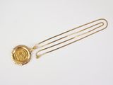 a gold necklace with a wax seal on it