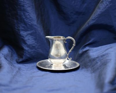 a silver pitcher sitting on a saucer on a blue cloth