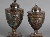 pair of antique silverplated urns on pedestals on grey background