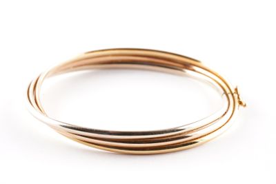 deux bracelets rigides en or posés sur une surface blanche, sur fond blanc