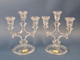 two clear glass candelabs with candles on a blue background