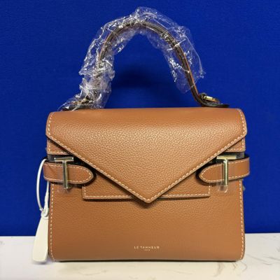 a tan leather handbag with a clear plastic handle on a table
