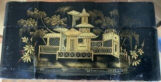 une boîte peinte en noir et or, sur laquelle est représenté un bâtiment