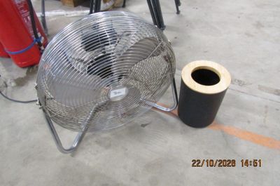 un ventilateur en métal posé par terre à côté d'un rouleau de ruban adhésif