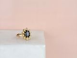 une bague en or sertie d'un saphir bleu, posée sur un bloc de marbre blanc