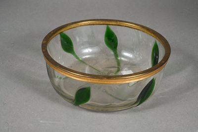 a glass bowl with a gold rim and green leaves on it