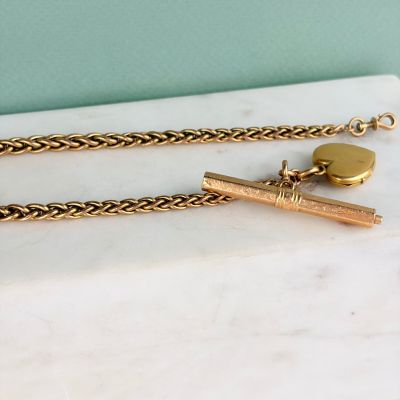 collier plaqué or composé d'une chaîne en or et d'un stylo posé sur une surface en marbre