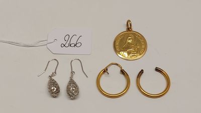 trois paires de boucles d'oreilles et une pièce d'or posées sur une surface blanche