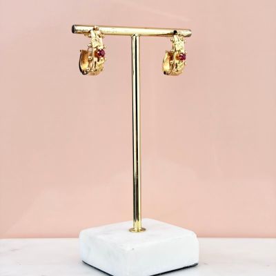 une paire de boucles d'oreilles en or posée sur un socle en marbre, devant un mur rose