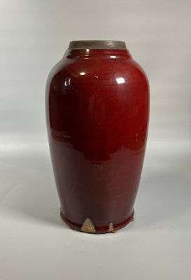 un vase rouge posé sur une surface blanche