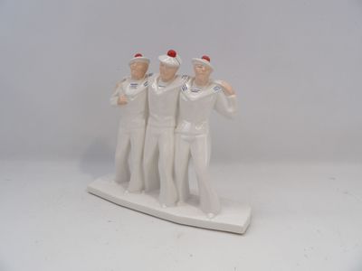 trois figurines de marins posées sur un socle blanc