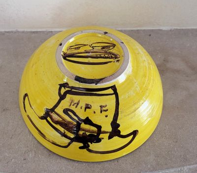 un bol jaune orné d'un dessin, posé par terre