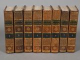 six old books are lined up in a row on a gray surface