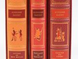 Trois livres sont posés sur une surface blanche ; l'un est rouge et l'autre est doré.