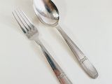 two silver spoons and a fork on a white table